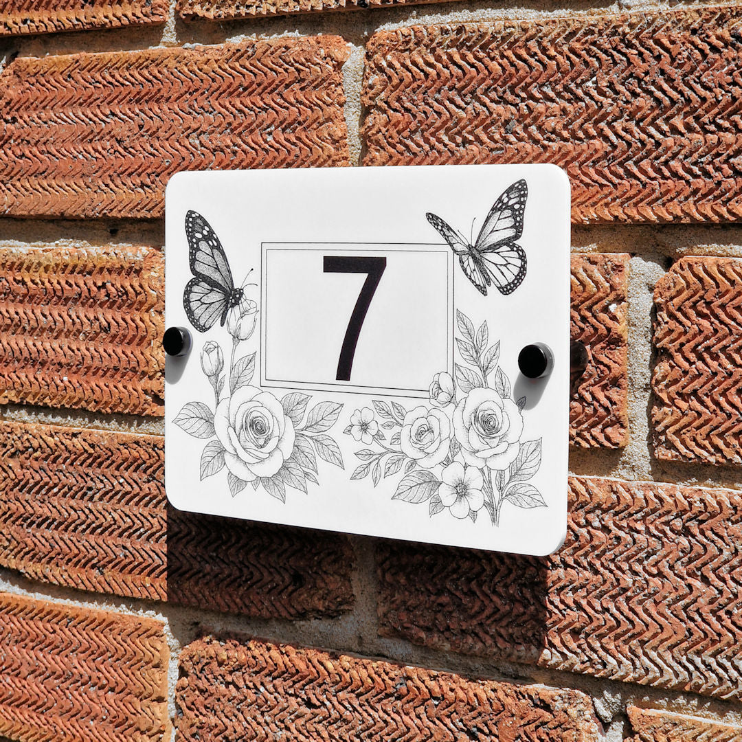 Decorative house number sign with butterflies and flowers on a brick wall.