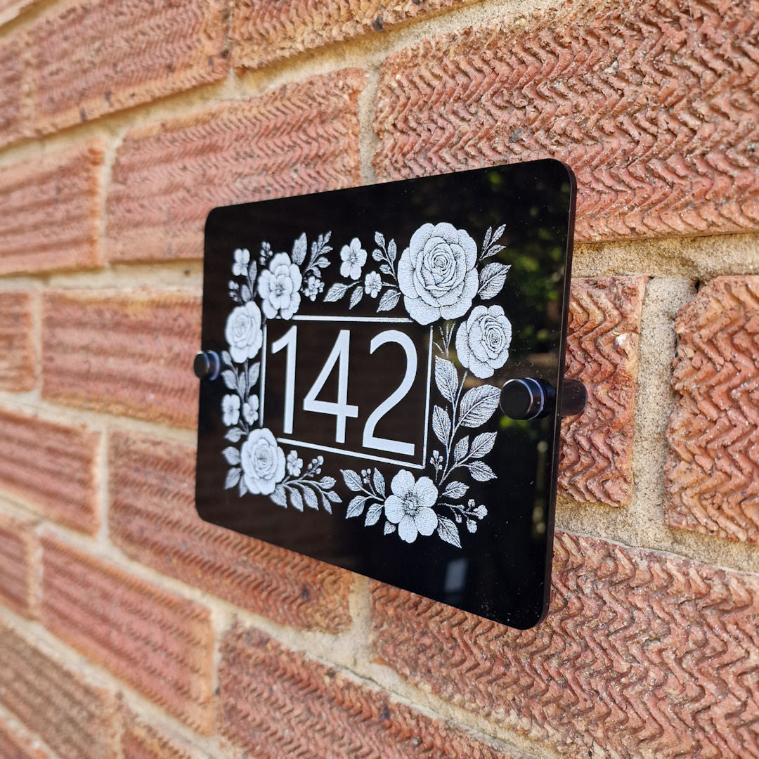 House number sign with floral border design on a brick wall