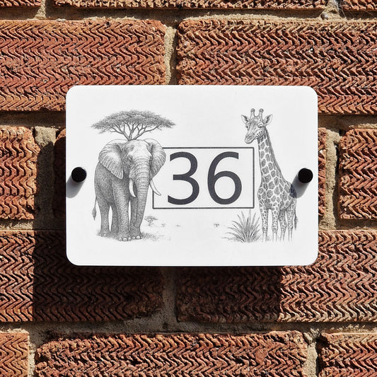 Decorative house number sign with elephant, giraffe, and tree design on a brick wall.