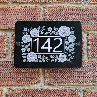 Decorative house number sign with floral border on a brick wall
