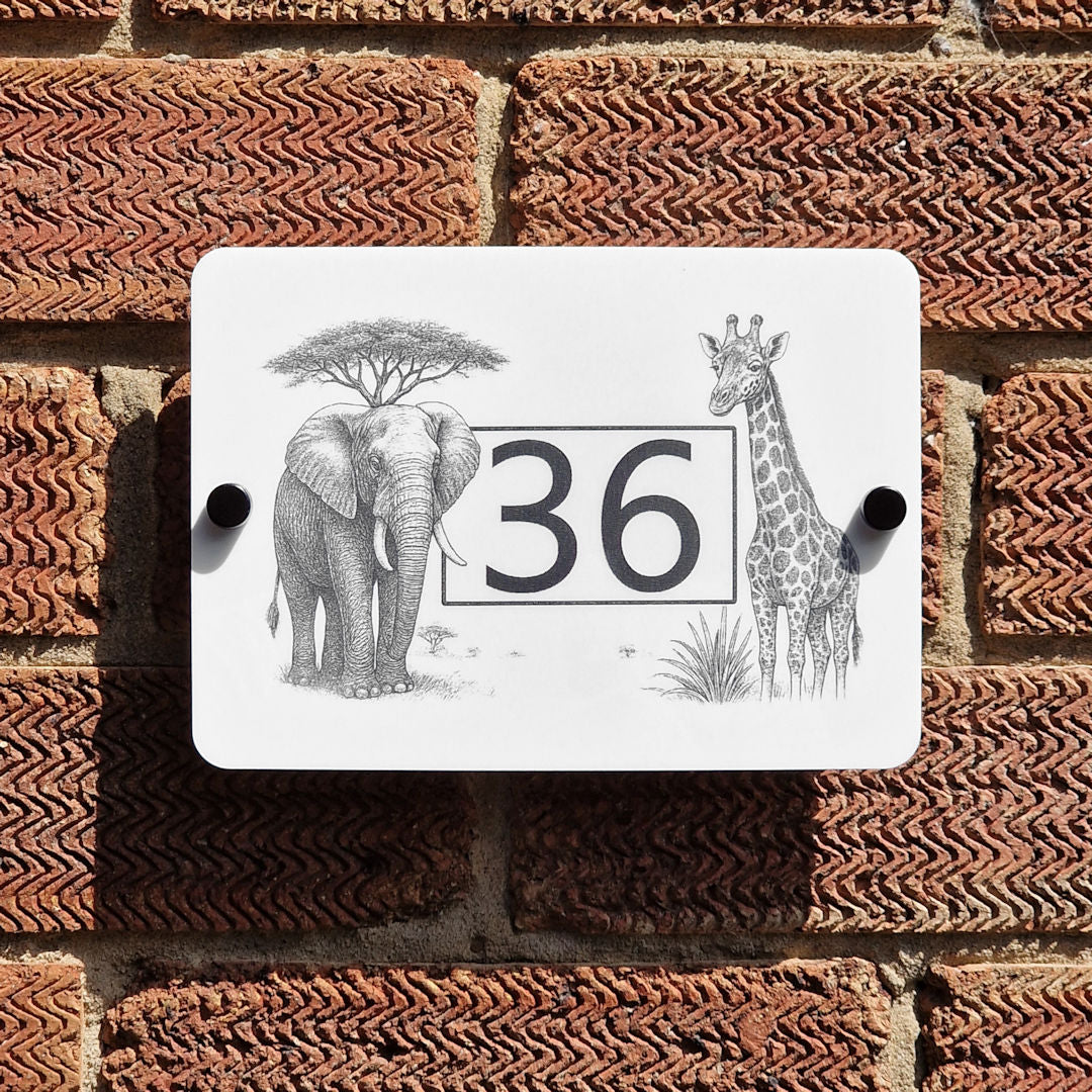 Decorative house number sign with elephant, giraffe, and tree design on a brick wall.