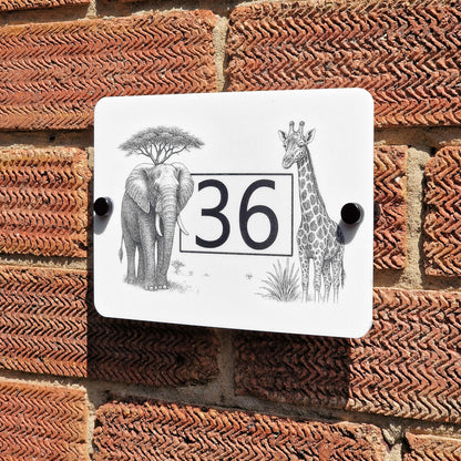 Decorative house number sign with elephant and giraffe design on a brick wall.